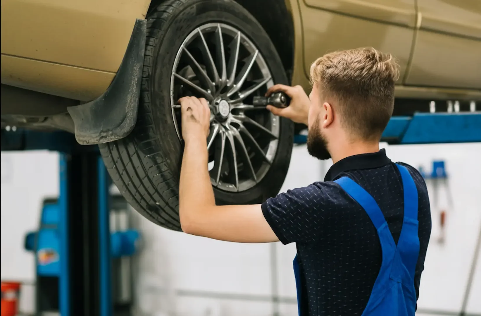 Best tire shops: A professional mechanic in blue overalls kneeling to tighten lug nuts on a white SUV with an electric impact wrench, representing the high-quality service at the best tire shops.