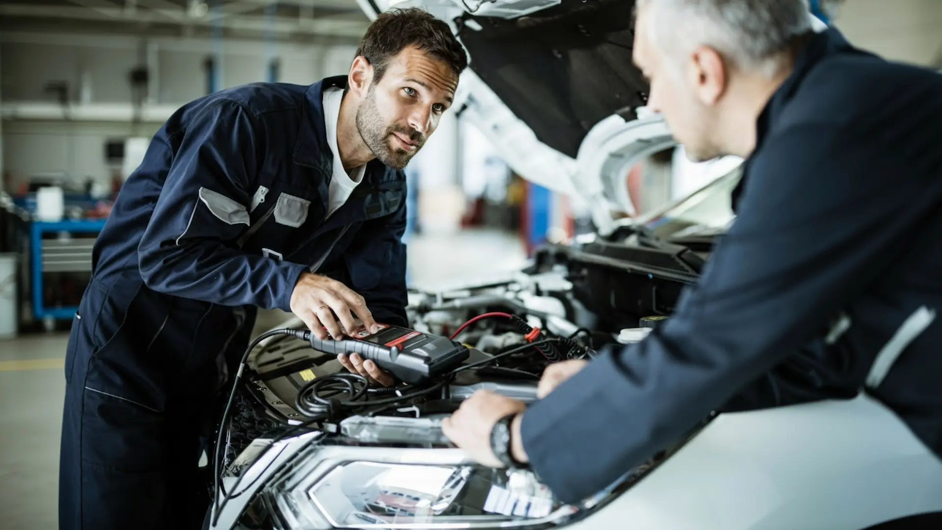 Affordable Car Repair: mechanics at Southport Auto Repair using a handheld diagnostic tool to troubleshoot an engine under the hood of a car.