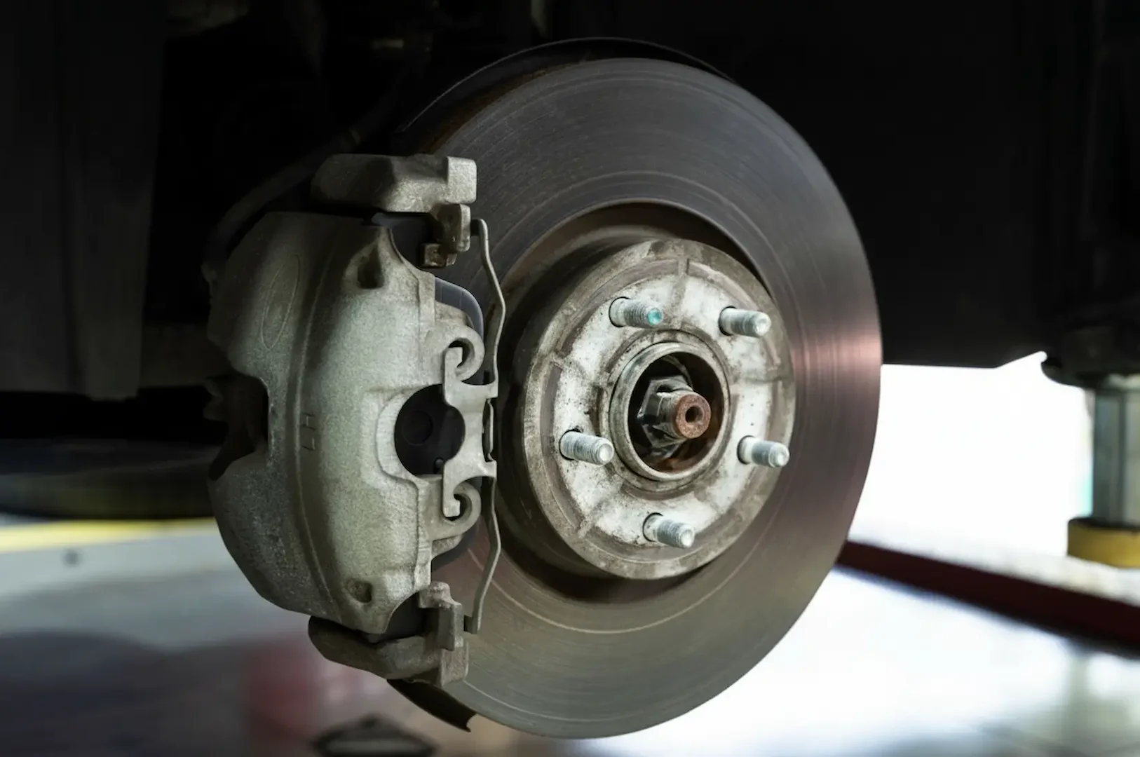 Brake replacement: Detailed close-up shot of an automotive disc brake caliper and rotor assembly mounted on a car.