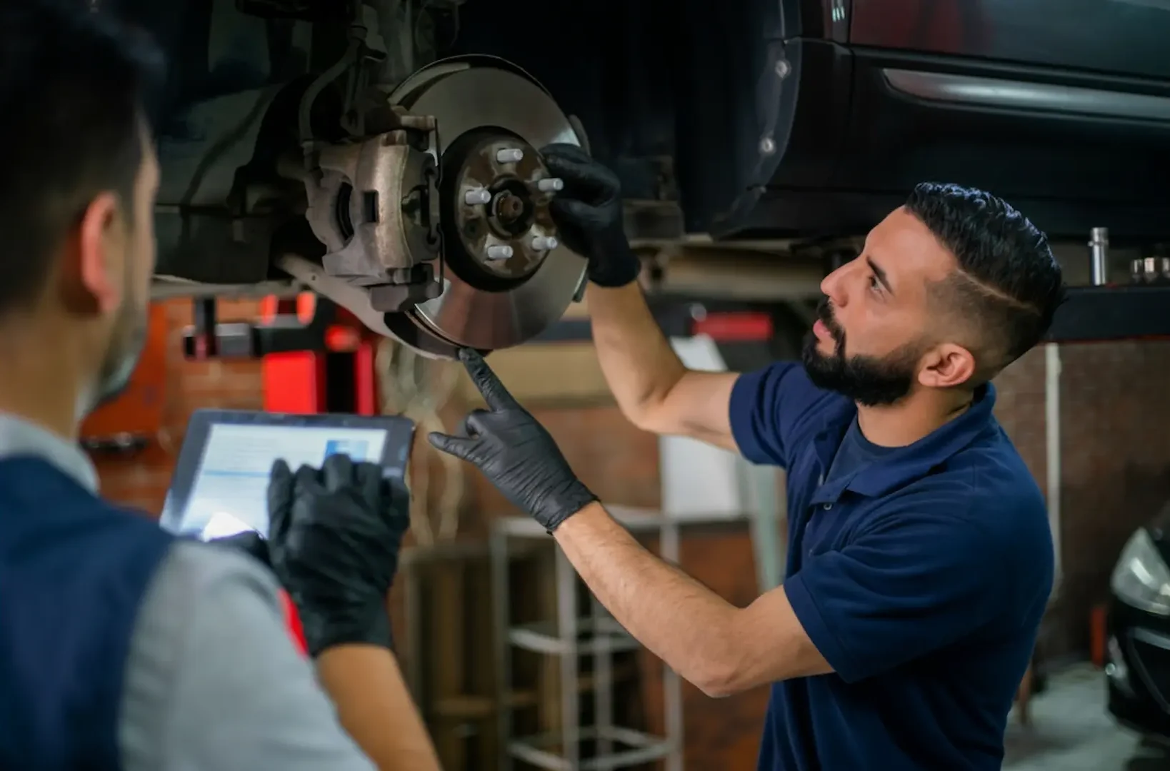 Expert mechanics at Southport Auto Repair inspecting a vehicle's disc brake rotor and caliper while using a digital tablet for diagnostics.