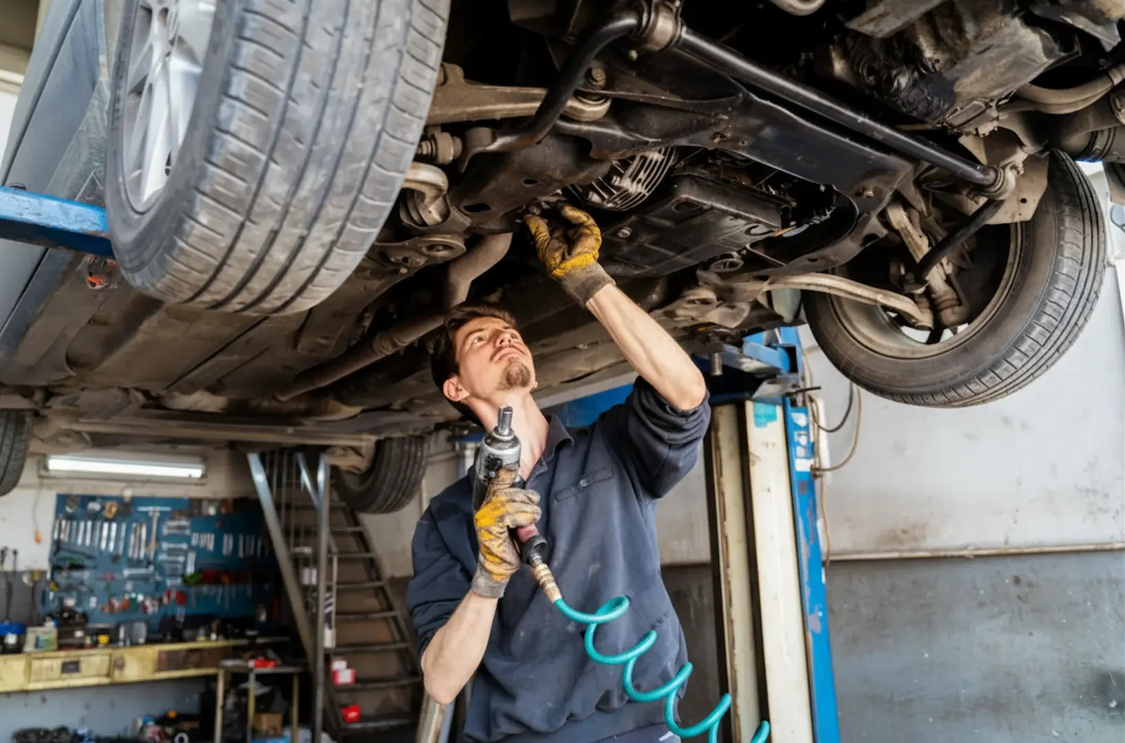 Affordable Car Repair: Technician in the workshop using a pneumatic tool to work on the underside of a vehicle raised for service.