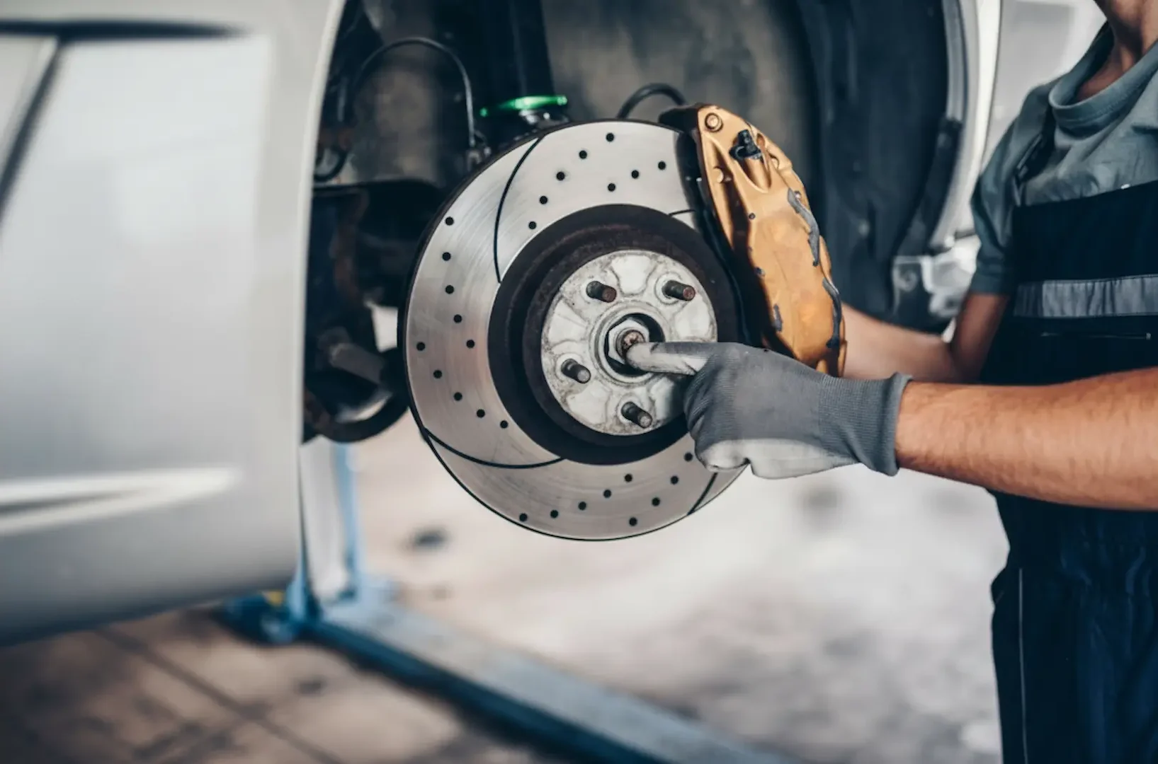 Brake replacement: A Close-up of a technician installing or inspecting a high-performance slotted and drilled brake rotor with a gold caliper.