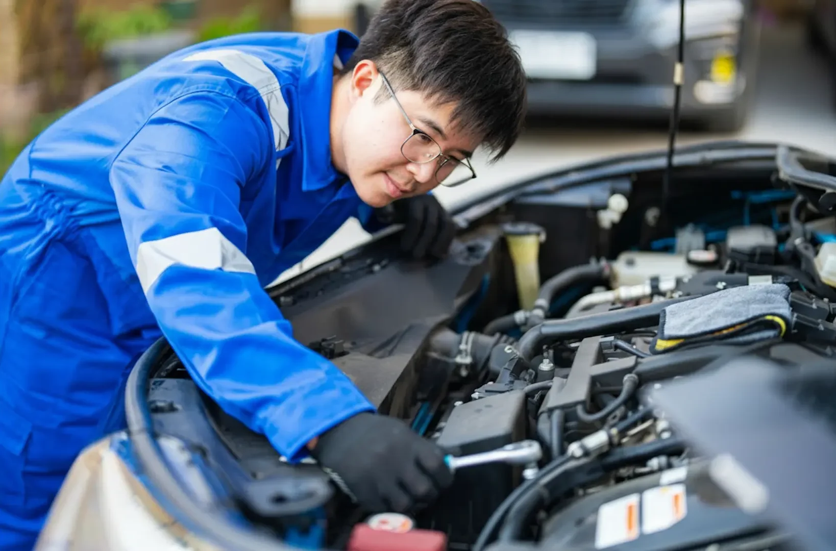 Mechanic Services: A male technician wearing glasses and blue workwear using a wrench to tighten bolts on a car engine.