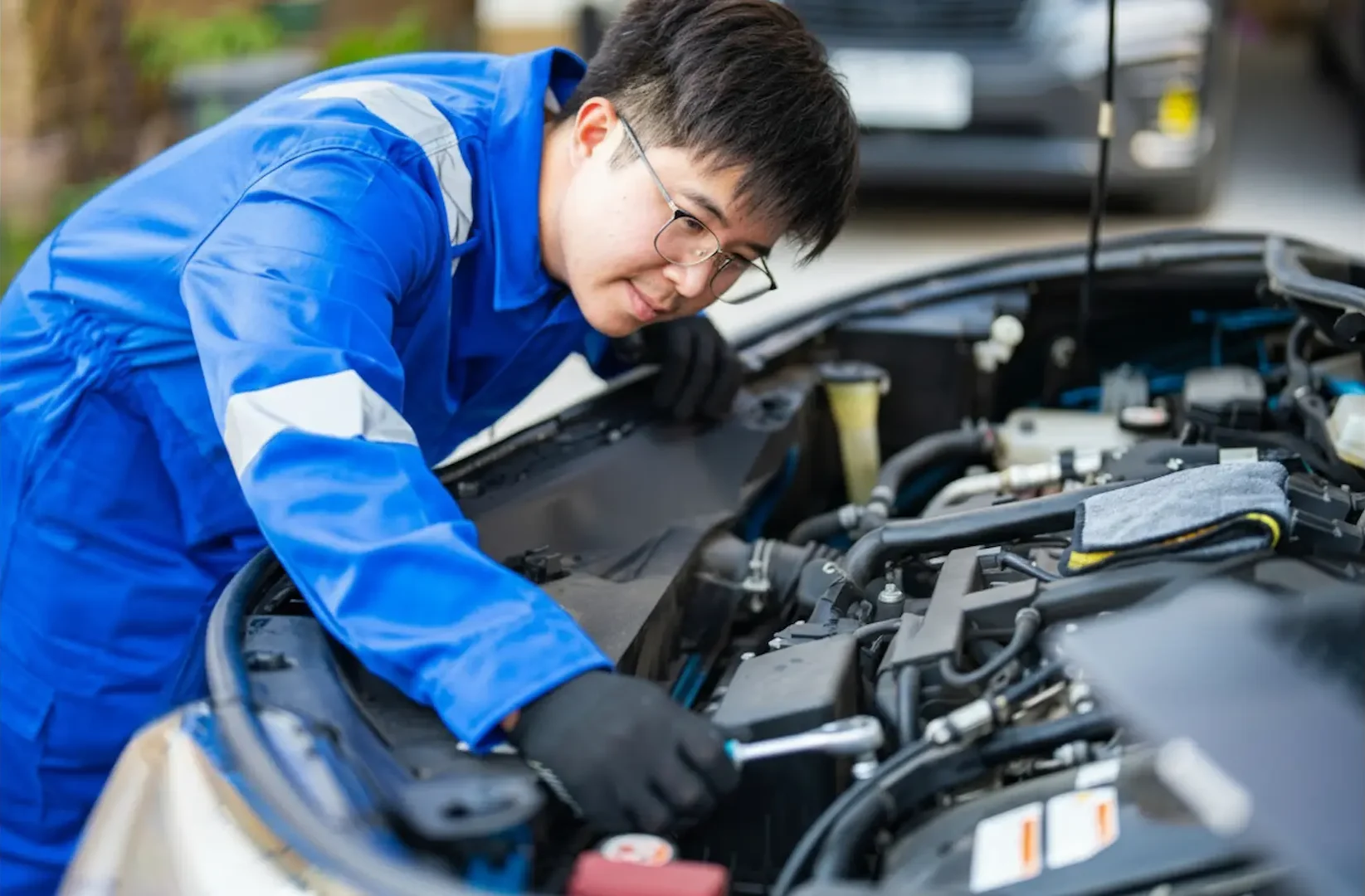 Affordable Car Repair: Mechanic in a blue uniform using a socket wrench to perform engine repairs in a clean, modern workshop.