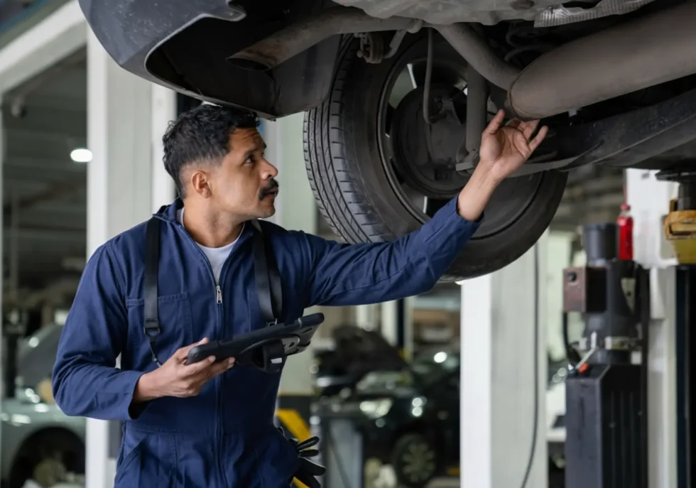 Brake repair Service: A mechanic working under a lifted vehicle to repair or adjust front suspension and axle components.