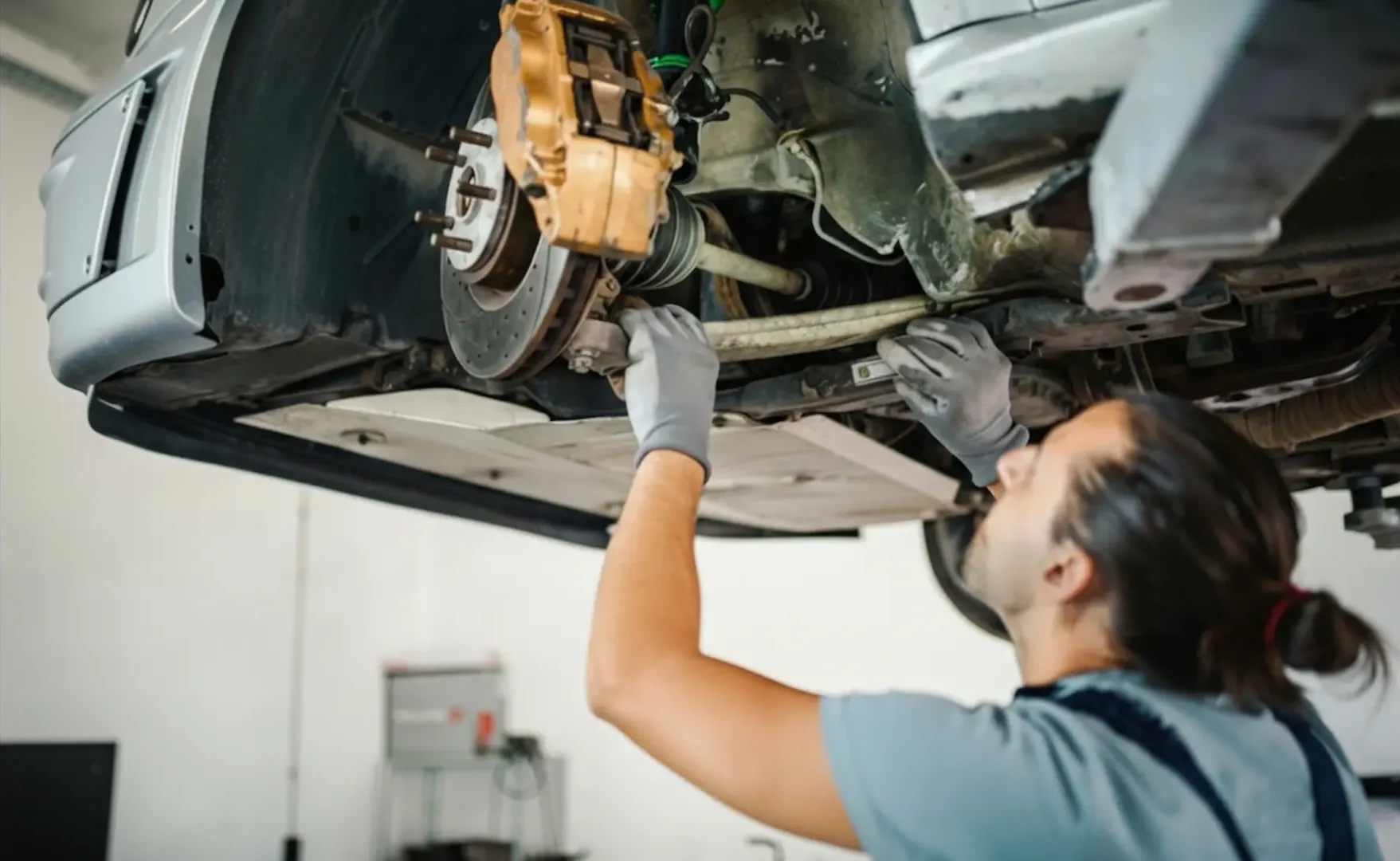Brake replacement: A mechanic working under a lifted vehicle to repair or adjust front suspension and axle components.