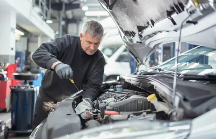 Immediate Repair : A senior mechanic in a black sweater checking the oil dipstick of a white vehicle in a professional garage.