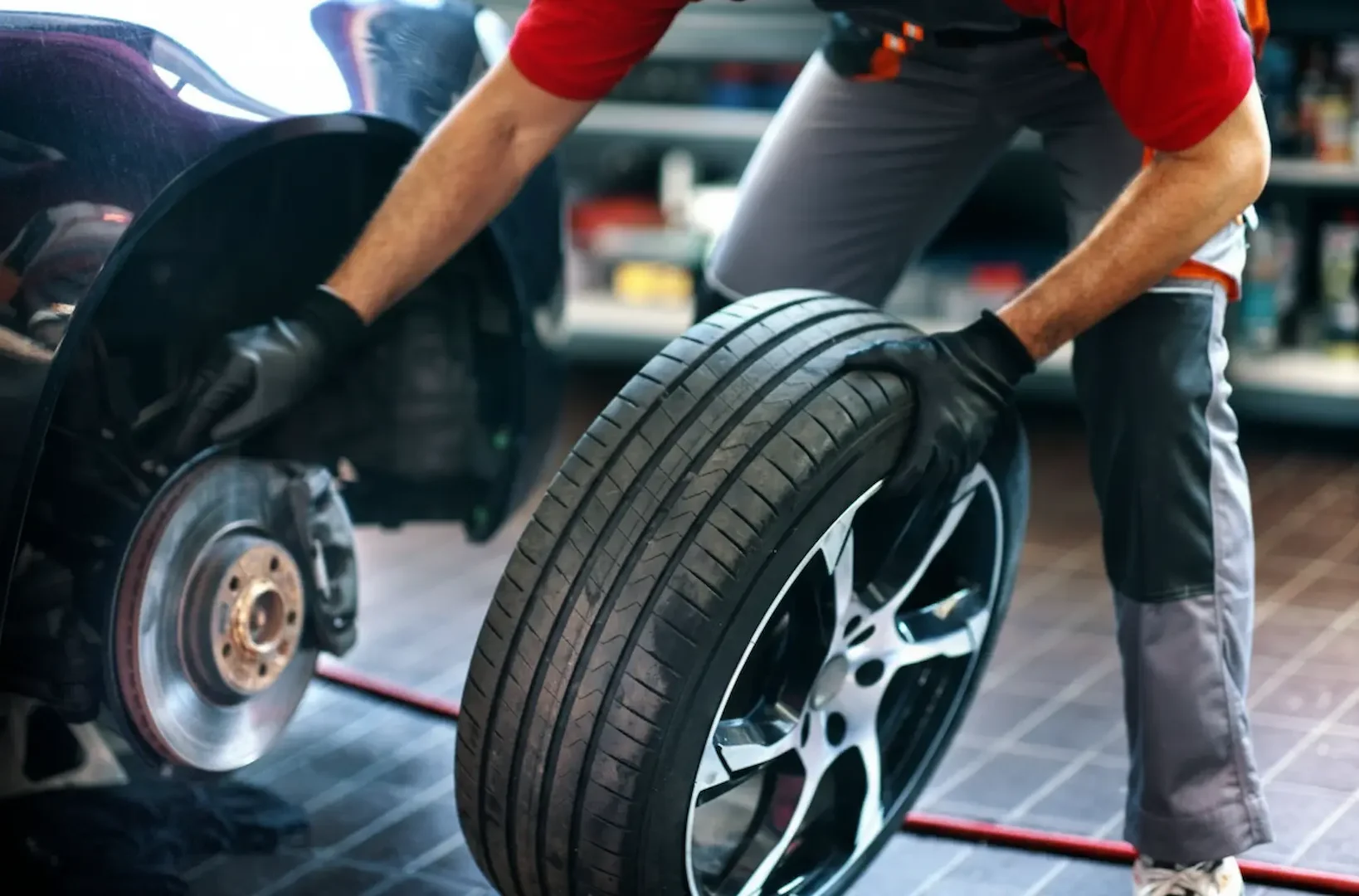 Affordable tire options: A mechanic in a red shirt and grey trousers installing a performance tire onto a vehicle's brake hub.