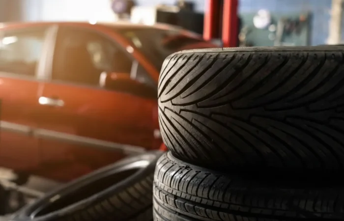 Affordable tire options: A stack of new tires with distinct tread patterns in an auto garage, with a blurred car in the background.