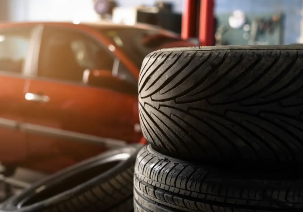 Affordable tire options: A stack of new tires with distinct tread patterns in an auto garage, with a blurred car in the background.
