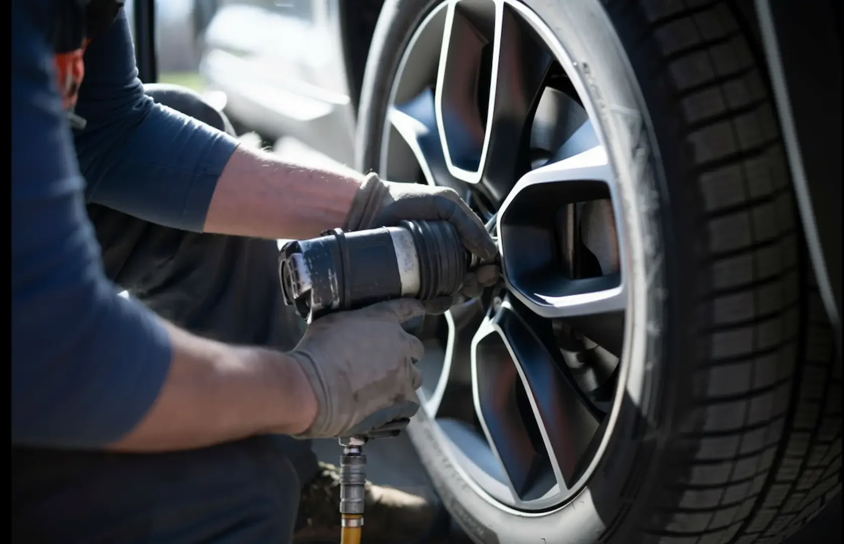 Affordable tire options: A close-up of a technician using a pneumatic impact wrench to remove lug nuts from a modern alloy wheel.