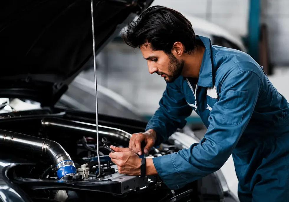 Mechanic performing a pre-purchase car inspection by examining a vehicle engine under an open hood in an auto repair garage.