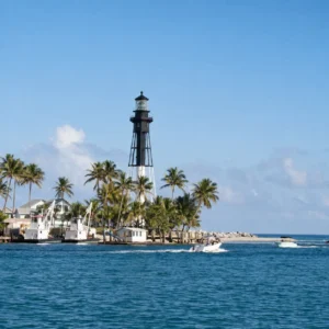 Hillsboro Inlet Lighthouse near Pompano Beach FL surrounded by palm trees, boats and turquoise coastal water