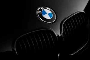 Dramatic close-up of a black BMW vehicle featuring the chrome-rimmed blue-and-white roundel emblem above the iconic dual kidney grilles.