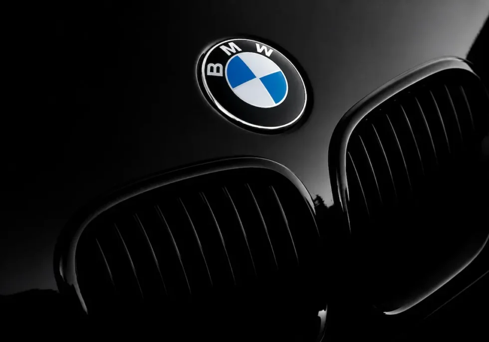 Dramatic close-up of a black BMW vehicle featuring the chrome-rimmed blue-and-white roundel emblem above the iconic dual kidney grilles.